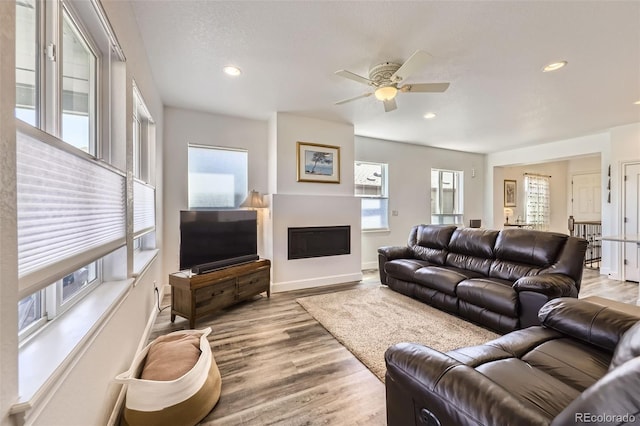 living area featuring wood finished floors, a fireplace, a ceiling fan, baseboards, and recessed lighting