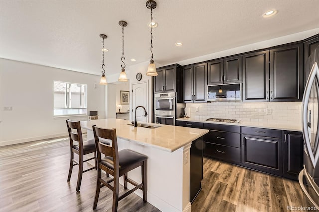 kitchen with a sink, appliances with stainless steel finishes, wood finished floors, light countertops, and a breakfast bar area