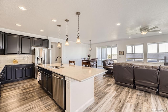 kitchen featuring appliances with stainless steel finishes, a sink, open floor plan, light wood-style floors, and decorative backsplash