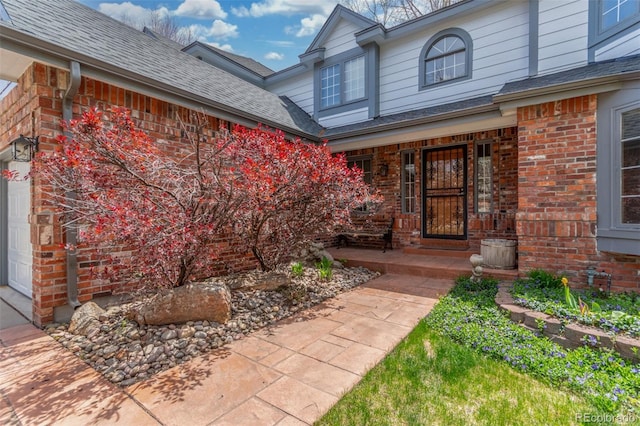 property entrance featuring a porch, a shingled roof, and brick siding