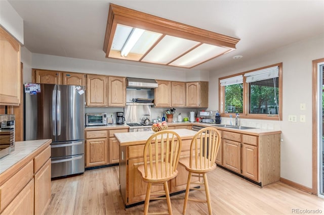 kitchen with freestanding refrigerator, a sink, a kitchen island, tile counters, and light wood-type flooring