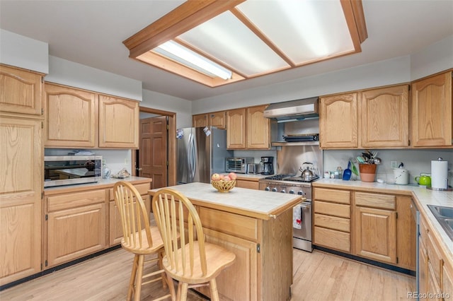 kitchen featuring a center island, a kitchen bar, wall chimney exhaust hood, light wood-style floors, and stainless steel appliances