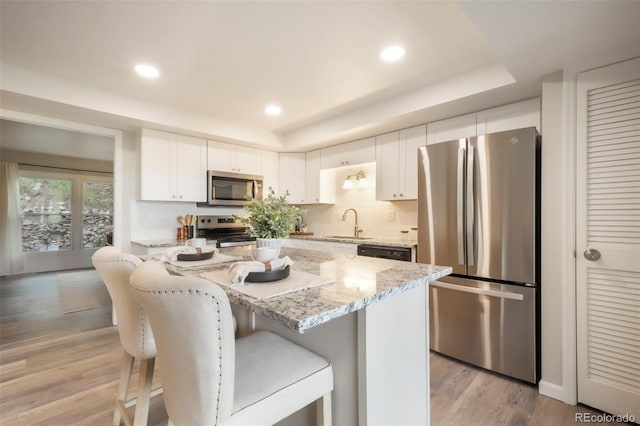 404 Raspberry Ln, Monument, CO 80132 - kitchen featuring appliances with stainless steel finishes, a tray ceiling, light stone counters, a kitchen breakfast bar, and recessed lighting
