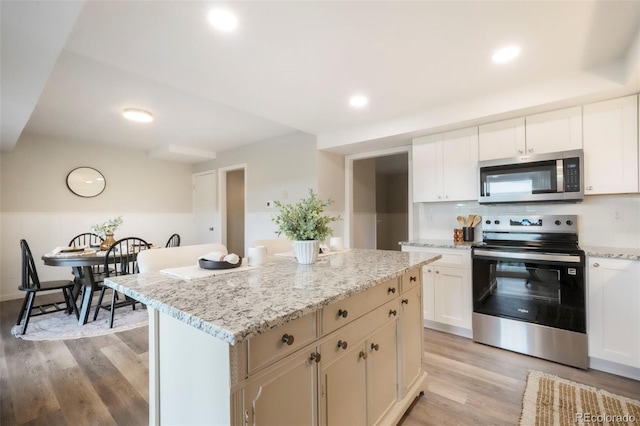 404 Raspberry Ln, Monument, CO 80132 - kitchen with stainless steel appliances, light wood-style flooring, a center island, white cabinets, and light stone counters