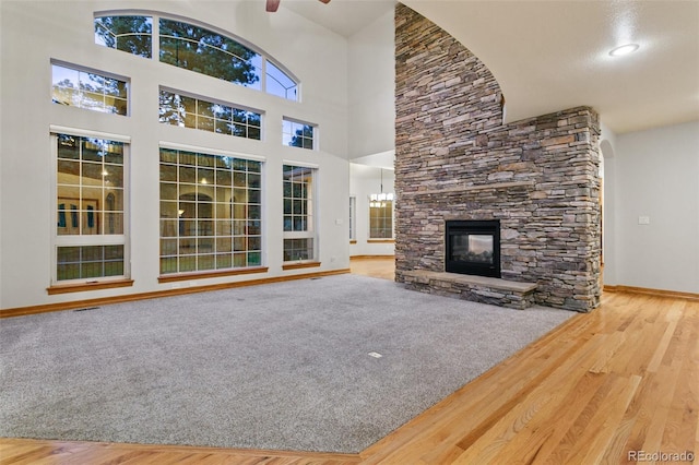 unfurnished living room featuring a high ceiling, carpet flooring, a fireplace, and ceiling fan with notable chandelier