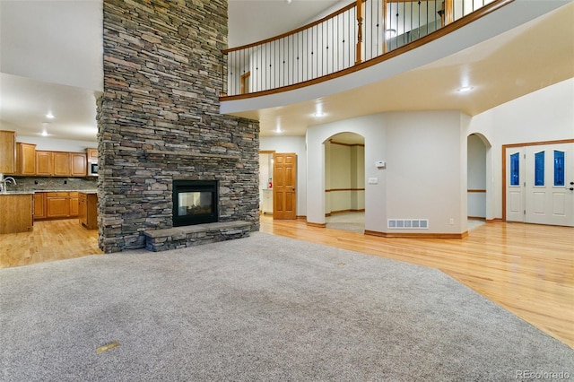 living room with a towering ceiling, a stone fireplace, and light wood-type flooring