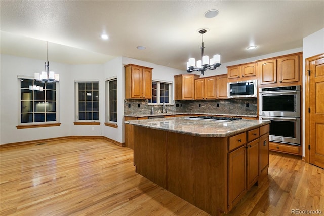 kitchen featuring tasteful backsplash, stainless steel appliances, decorative light fixtures, light wood-type flooring, and a center island