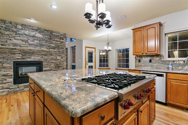 kitchen with a fireplace, light wood-type flooring, a kitchen island, pendant lighting, and tasteful backsplash