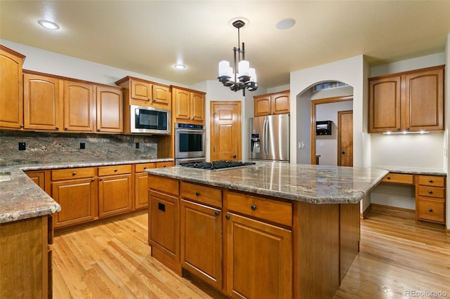 kitchen with light hardwood / wood-style floors, hanging light fixtures, a kitchen island, stainless steel appliances, and backsplash