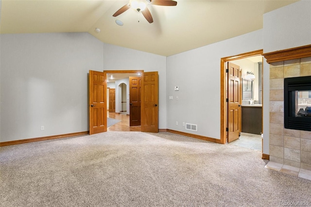 unfurnished bedroom featuring ceiling fan, a fireplace, carpet, high vaulted ceiling, and connected bathroom