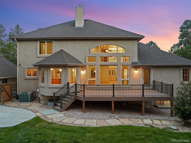 back house at dusk with a patio, a lawn, central AC unit, and a deck