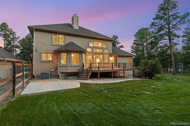 back house at dusk featuring a yard, central AC, a wooden deck, and a patio