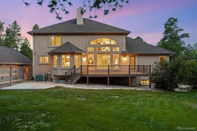 back house at dusk featuring a deck, central AC unit, and a lawn