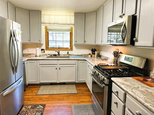 kitchen featuring sink, light wood-type flooring, light stone counters, and stainless steel appliances