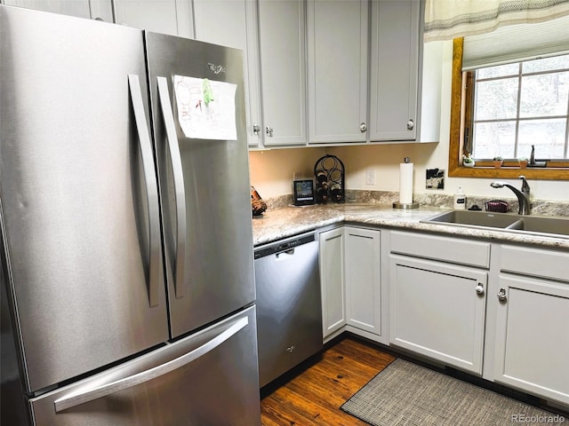 kitchen with appliances with stainless steel finishes, dark wood finished floors, light countertops, and a sink