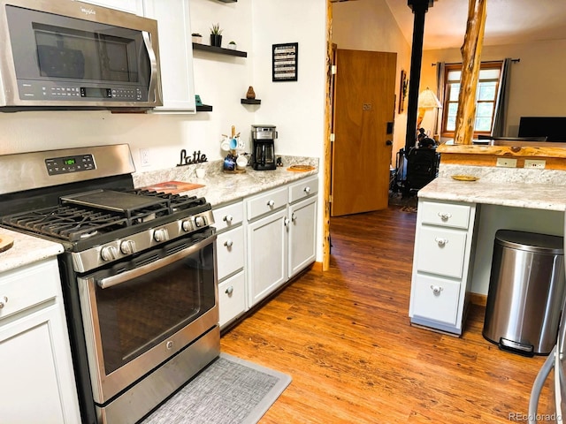 kitchen with appliances with stainless steel finishes, light stone countertops, light wood-style floors, white cabinetry, and open shelves