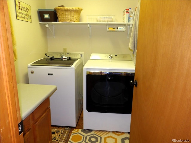 laundry room featuring wood-type flooring, washer and clothes dryer, and cabinets