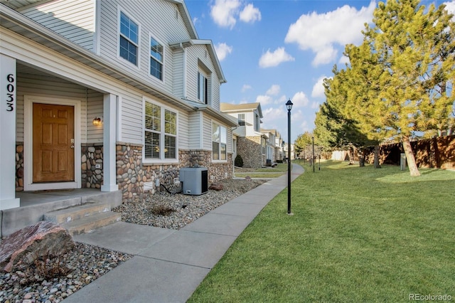 exterior space featuring stone siding, central AC, a residential view, and a lawn