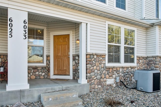 doorway to property featuring a porch, stone siding, and central AC