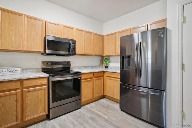 kitchen with light stone counters, appliances with stainless steel finishes, light brown cabinets, and light wood-style flooring