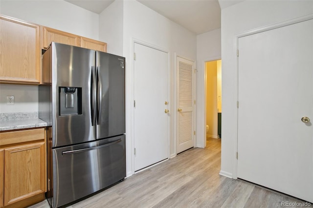 kitchen with stainless steel refrigerator with ice dispenser, light hardwood / wood-style floors, light stone counters, and light brown cabinets