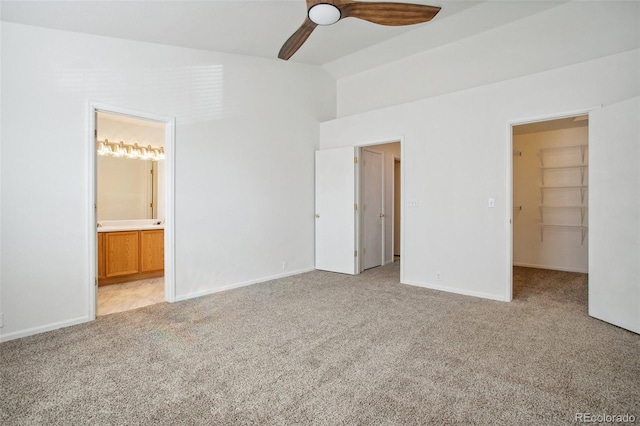 unfurnished bedroom featuring vaulted ceiling, ensuite bathroom, a walk in closet, ceiling fan, and light carpet