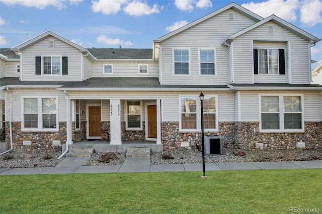 view of front facade featuring stone siding, cooling unit, covered porch, and a front lawn