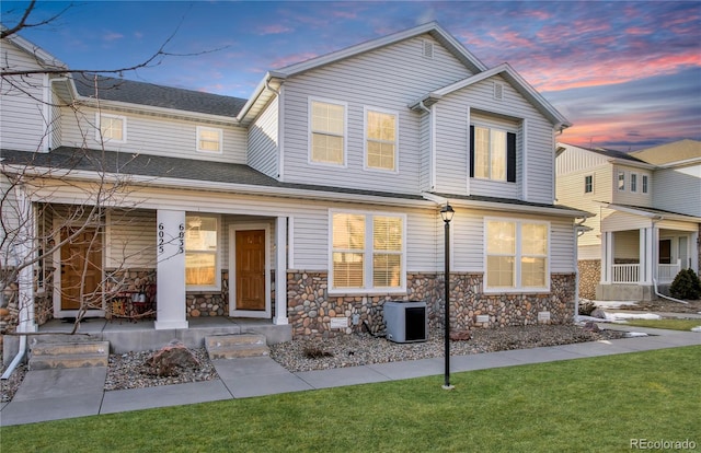 view of front of house featuring covered porch, stone siding, and a lawn