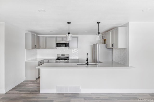 kitchen with hanging light fixtures, appliances with stainless steel finishes, gray cabinetry, and kitchen peninsula