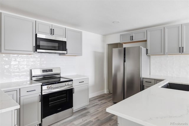 kitchen featuring tasteful backsplash, appliances with stainless steel finishes, gray cabinets, and light wood-type flooring