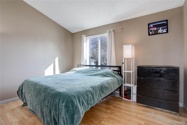 bedroom featuring vaulted ceiling, a textured ceiling, and light wood-type flooring