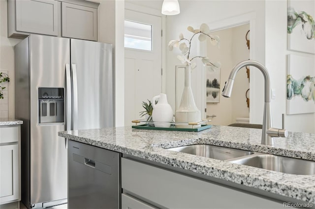 kitchen featuring a sink, appliances with stainless steel finishes, gray cabinetry, and light stone counters