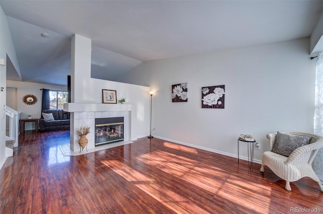 living room featuring a tiled fireplace, dark wood-type flooring, and vaulted ceiling