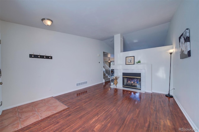 living room featuring a tiled fireplace, wood-type flooring, and vaulted ceiling