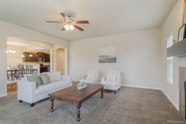 carpeted living room with a tiled fireplace and ceiling fan with notable chandelier