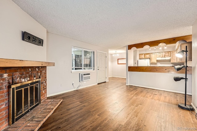 unfurnished living room with light wood-type flooring, a textured ceiling, an AC wall unit, and a brick fireplace