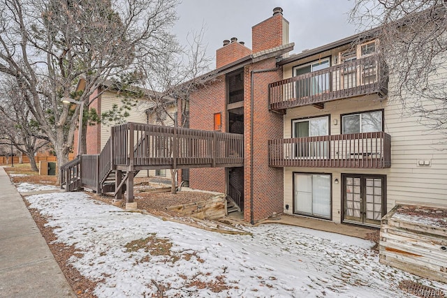 snow covered property featuring a balcony and a wooden deck