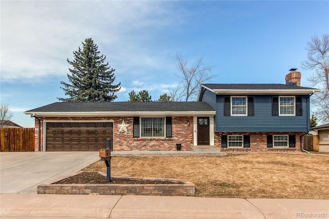 split level home with driveway, a chimney, an attached garage, fence, and brick siding