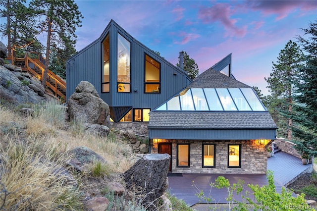 back of property at dusk featuring a shingled roof