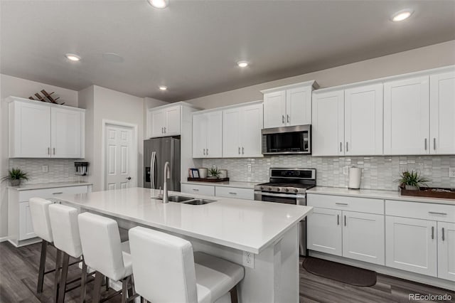 kitchen featuring white cabinets, sink, an island with sink, a kitchen bar, and stainless steel appliances