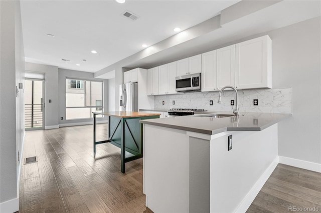 kitchen with appliances with stainless steel finishes, white cabinetry, decorative backsplash, kitchen peninsula, and hardwood / wood-style flooring