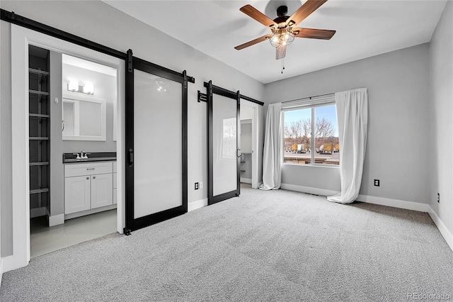 unfurnished bedroom with connected bathroom, light carpet, sink, ceiling fan, and a barn door