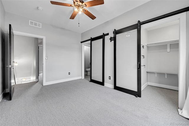 unfurnished bedroom featuring a closet, ceiling fan, light colored carpet, ensuite bathroom, and a barn door