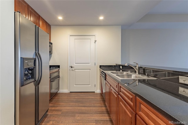 kitchen with dark wood finished floors, dark countertops, appliances with stainless steel finishes, brown cabinetry, and a sink