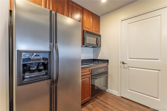 kitchen featuring dark countertops, black appliances, brown cabinets, and dark wood-type flooring