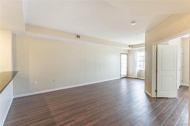 empty room with dark wood-style flooring, visible vents, and baseboards