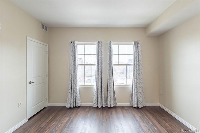 spare room with dark wood-style floors, visible vents, and baseboards