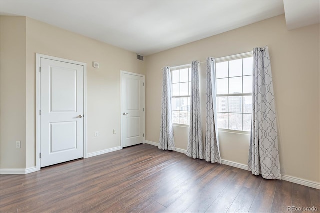 spare room featuring dark wood-style floors, visible vents, and baseboards