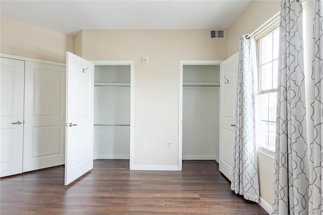 unfurnished bedroom with dark wood-style floors, visible vents, baseboards, and two closets