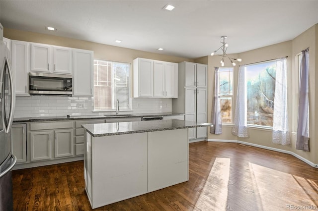 kitchen with pendant lighting, a center island, sink, light stone counters, and white cabinetry